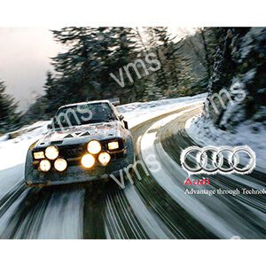 Classic Audi rally car racing on a snowy mountain road with bright headlights.