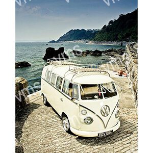 Vintage white Volkswagen van parked by a rocky beach with mountains in the background.
