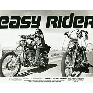 Two motorcyclists ride on chopper motorcycles in a black-and-white scene.