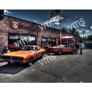 Two classic muscle cars parked outside a vintage garage at dusk.